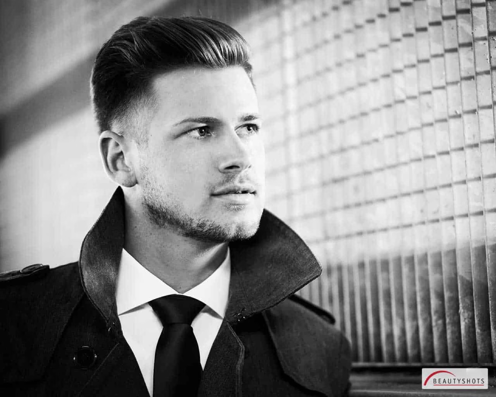 Schwarzweiß-Porträt eines Mannes im Mantel mit ernstem Blick – Männer-Fotoshooting