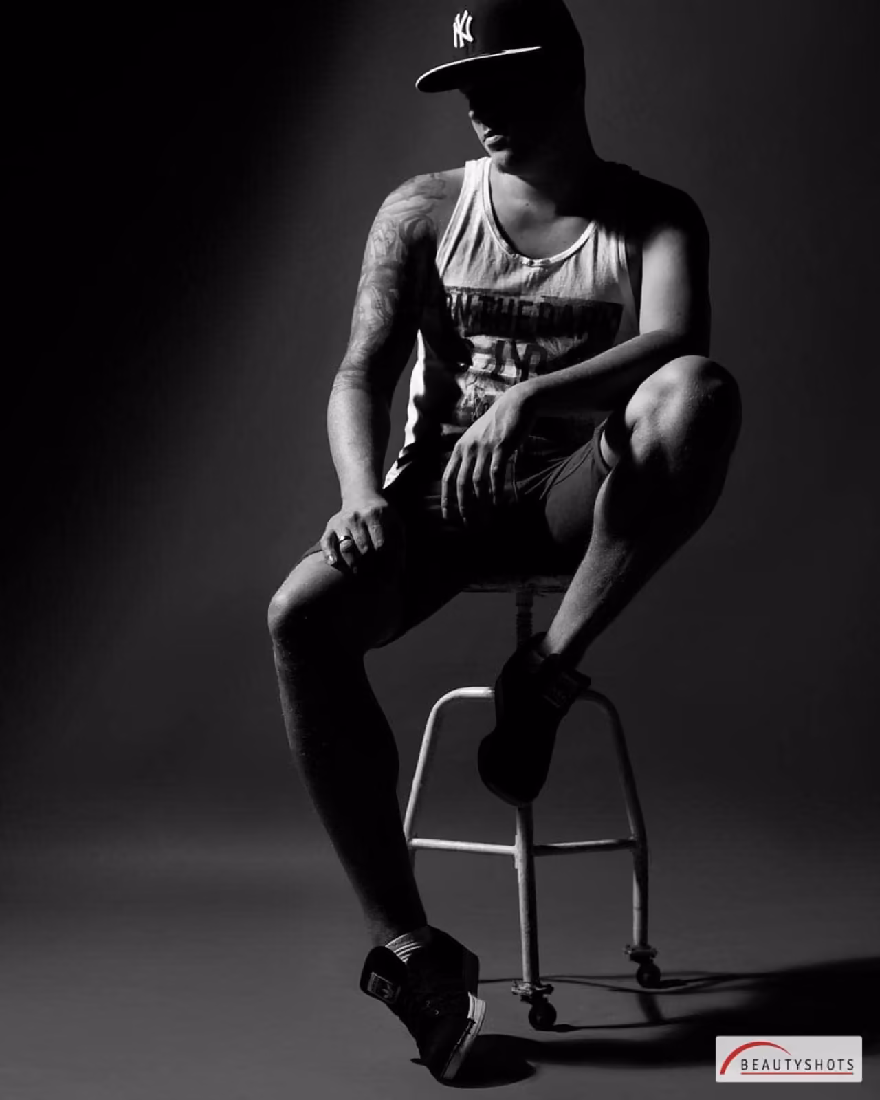 Mann im Tanktop auf einem Hocker vor dunklem Studiohintergrund