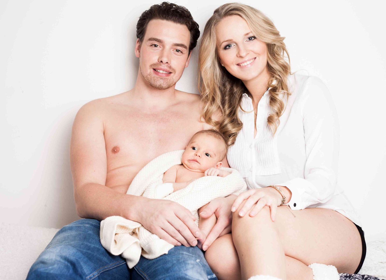 Eltern halten lächelnd ihr neugeborenes Baby im hellen Fotostudio in Hamburg