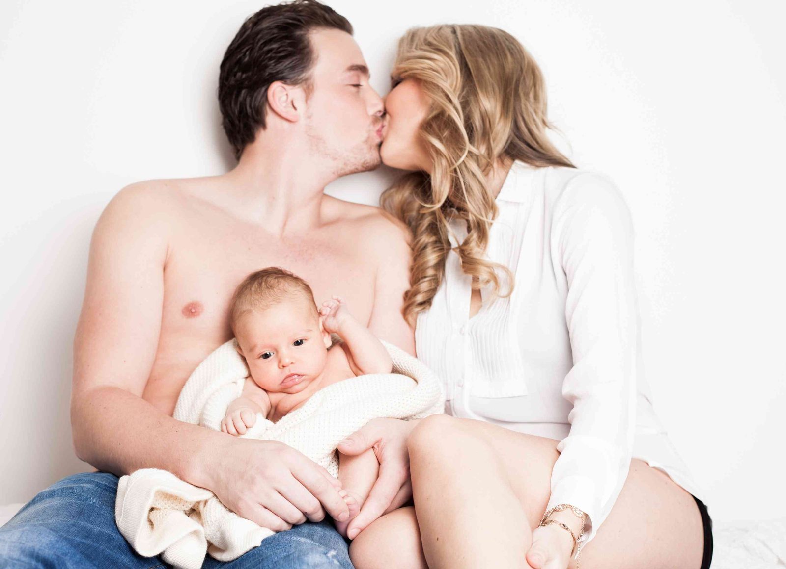 Paar küsst sich zärtlich, Mann hält Neugeborenes im Arm – Fotostudio in Hamburg