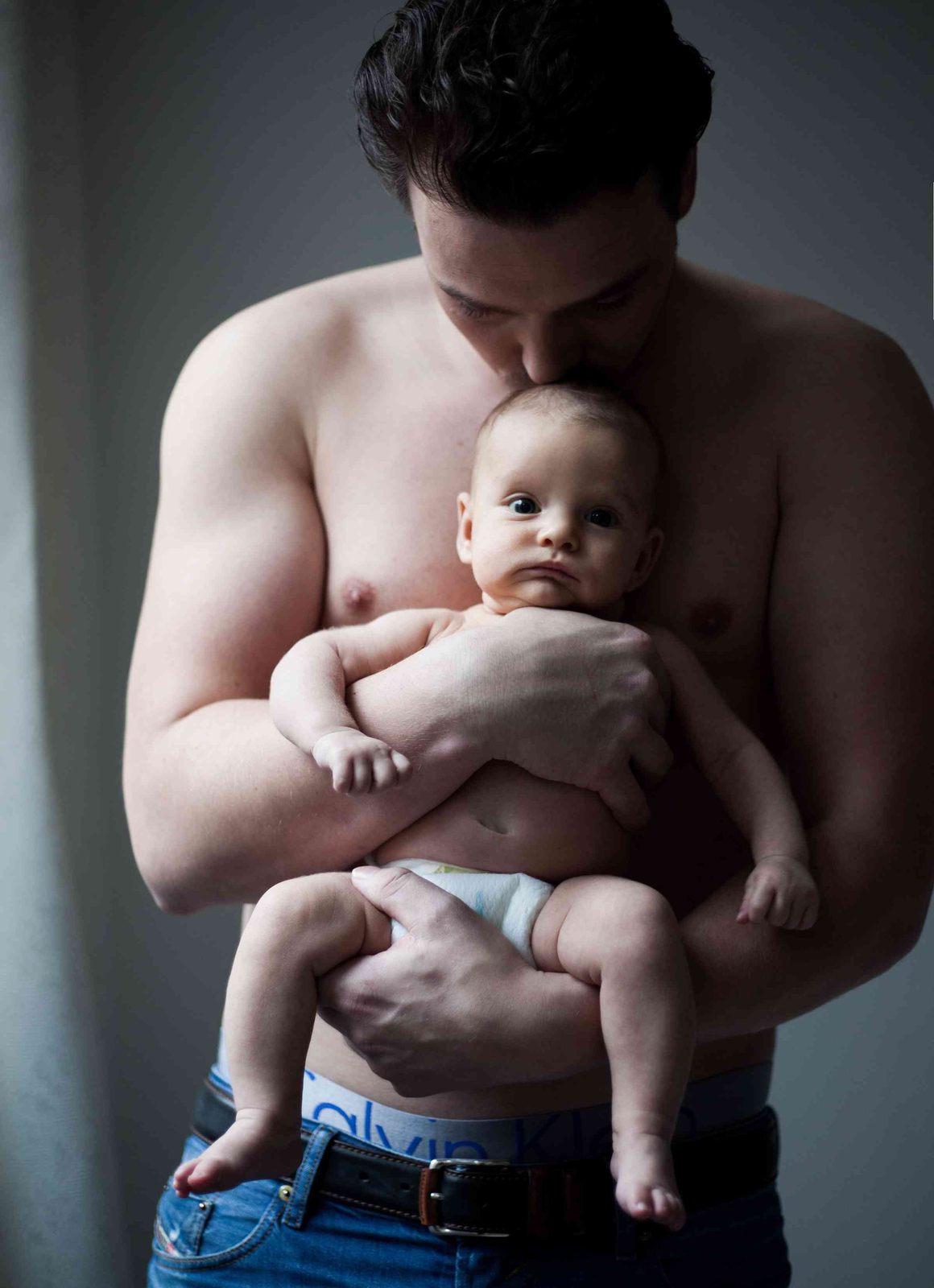 father kissing baby's head—tender portrait against a dark studio backdrop