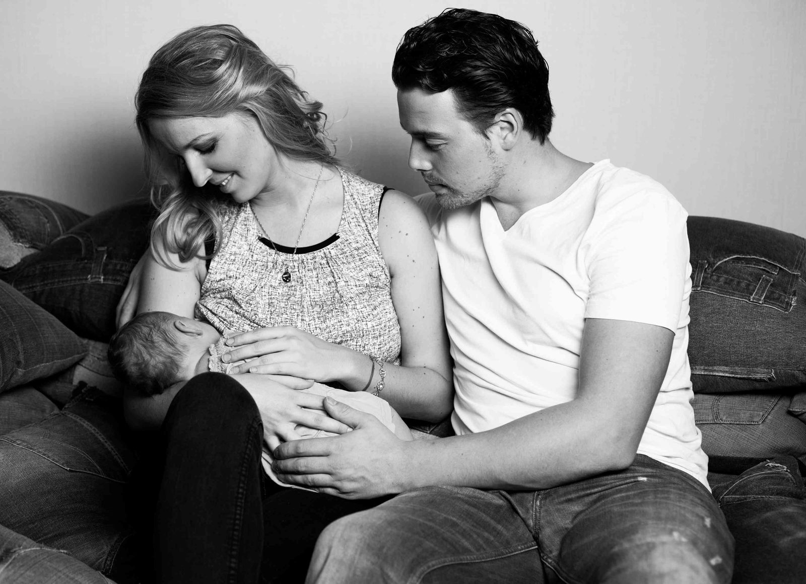Parents cradling their sleeping newborn together on a sofa