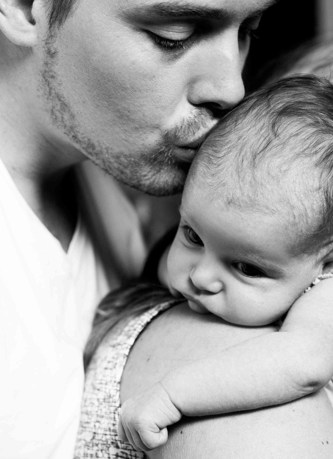 Father tenderly kisses baby's head in close-up black-and-white portrait