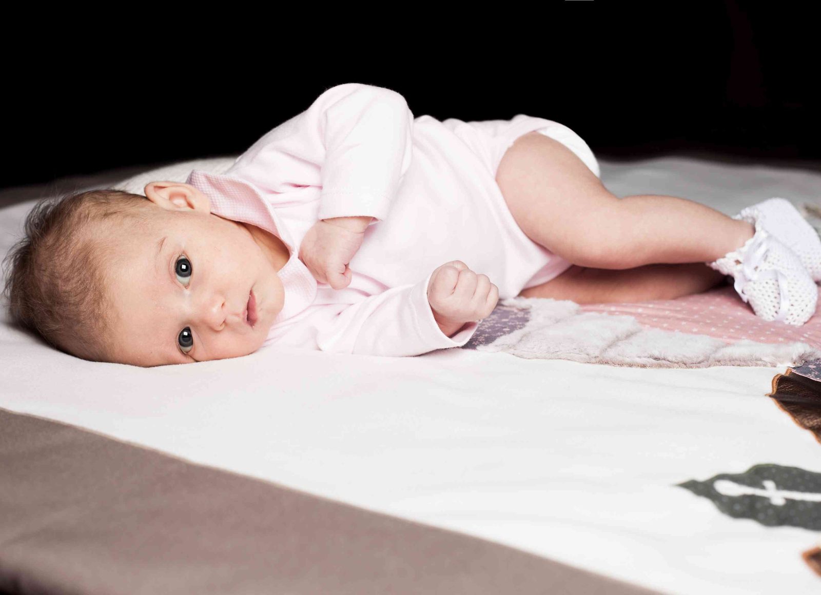 Baby in pink onesie lying on blanket against dark background