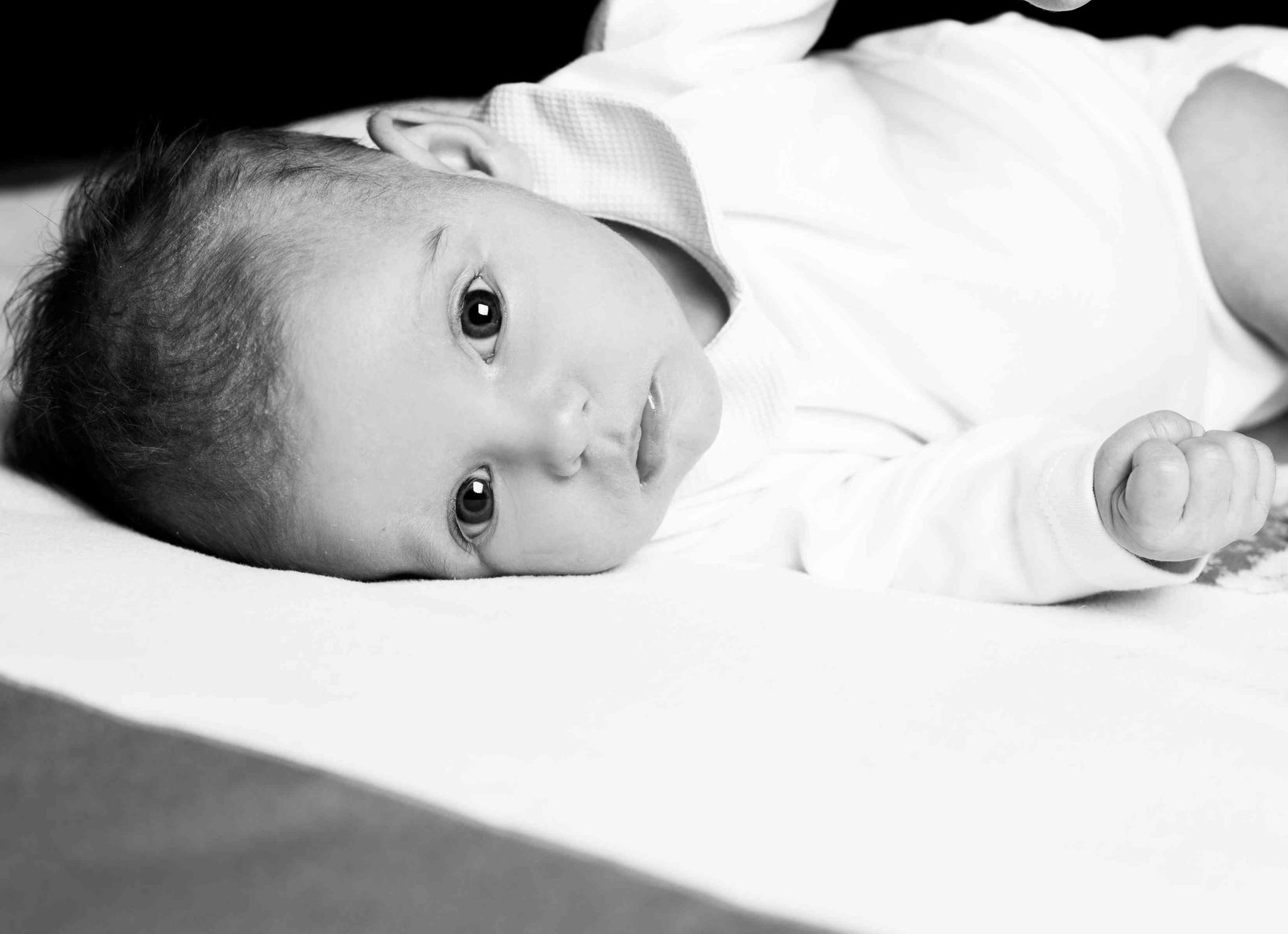 Baby in Schwarz-Weiß liegt auf weißer Decke und blickt in die Kamera