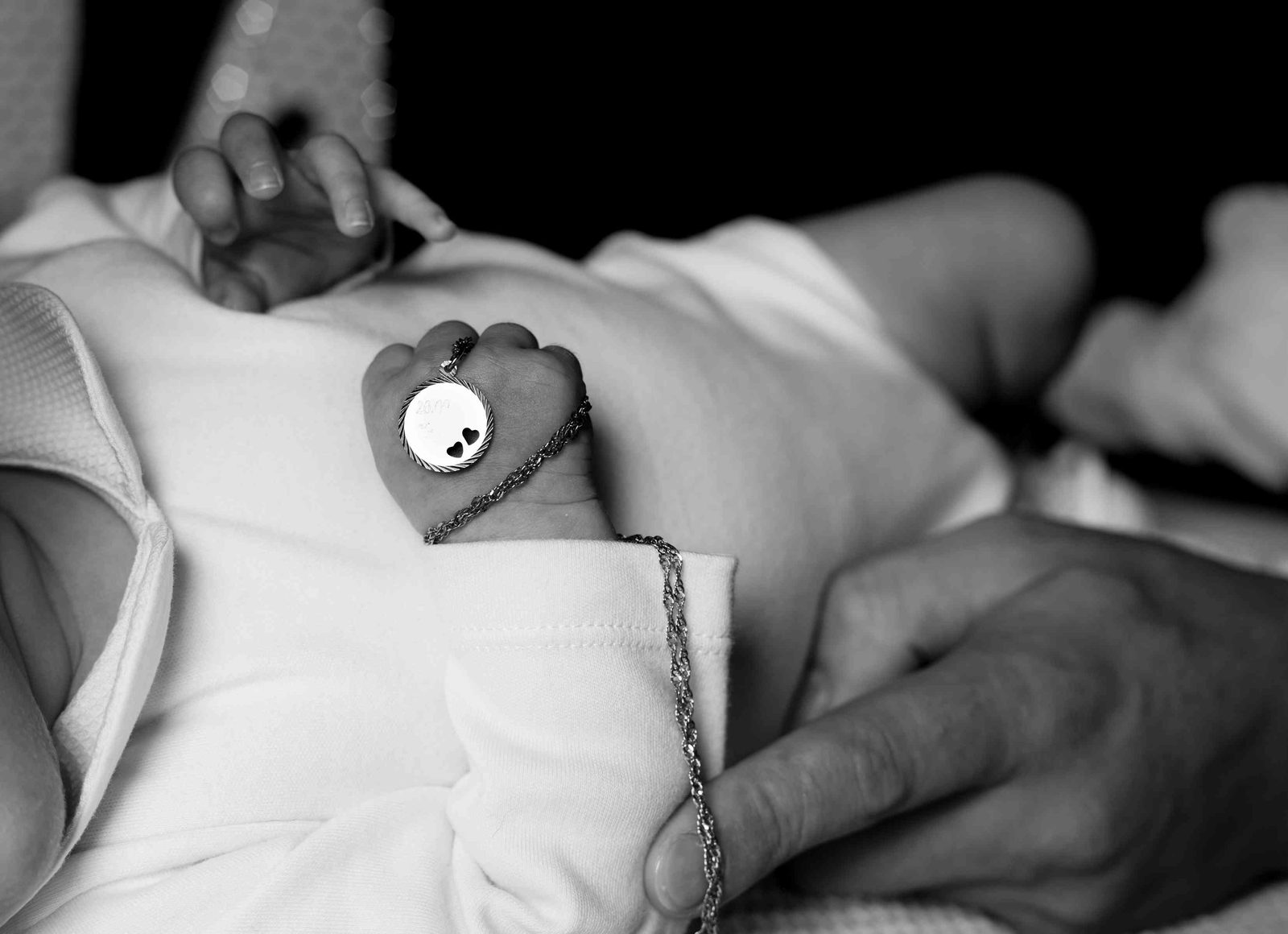 Baby hält Medaillon-Anhänger an Kette, Erwachsenenhand im Bild – Schwarz-weiß Nahaufnahme