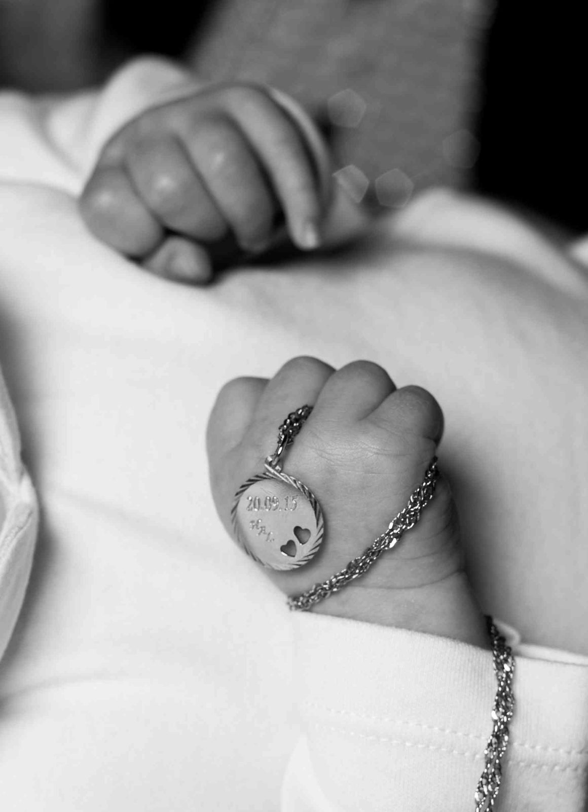 Babyhand hält gravierten Anhänger mit Datum – Schwarz-Weiß-Nahaufnahme