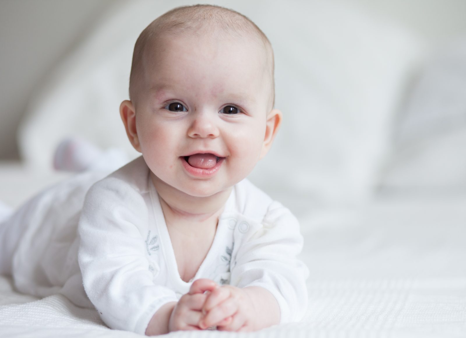 Smiling baby lies on a white bed, looking at the camera