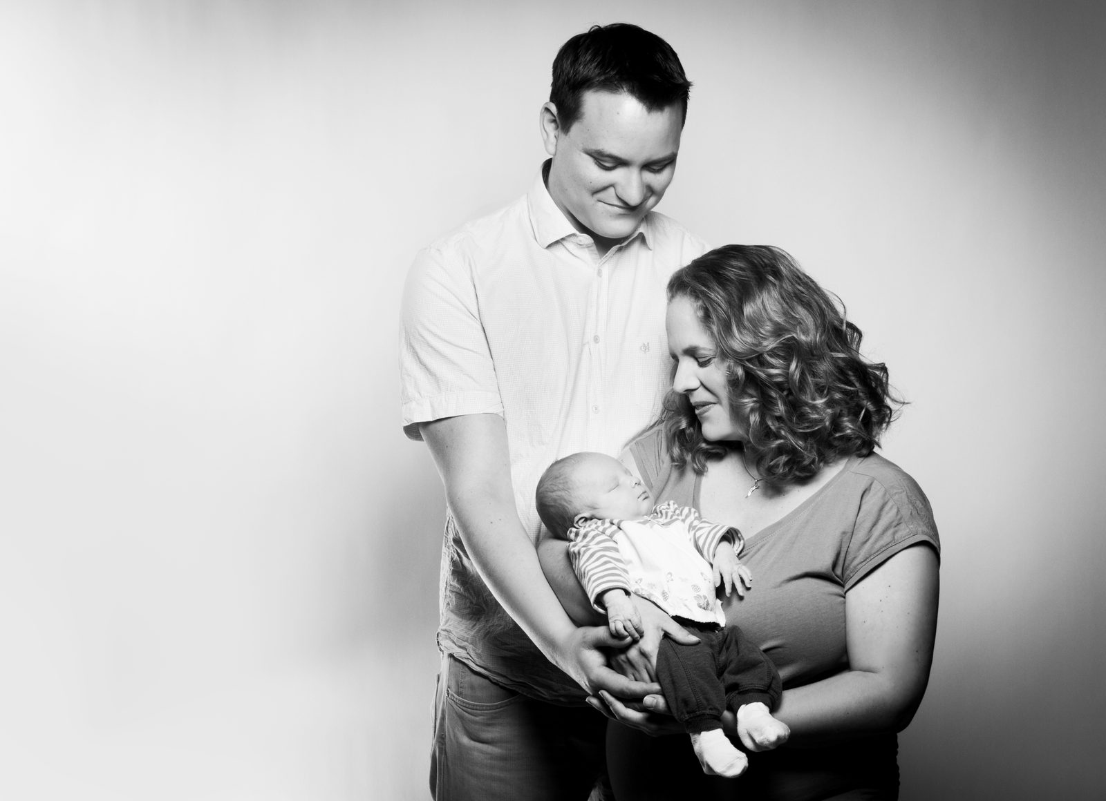 Parents smile tenderly while holding their newborn baby in the studio