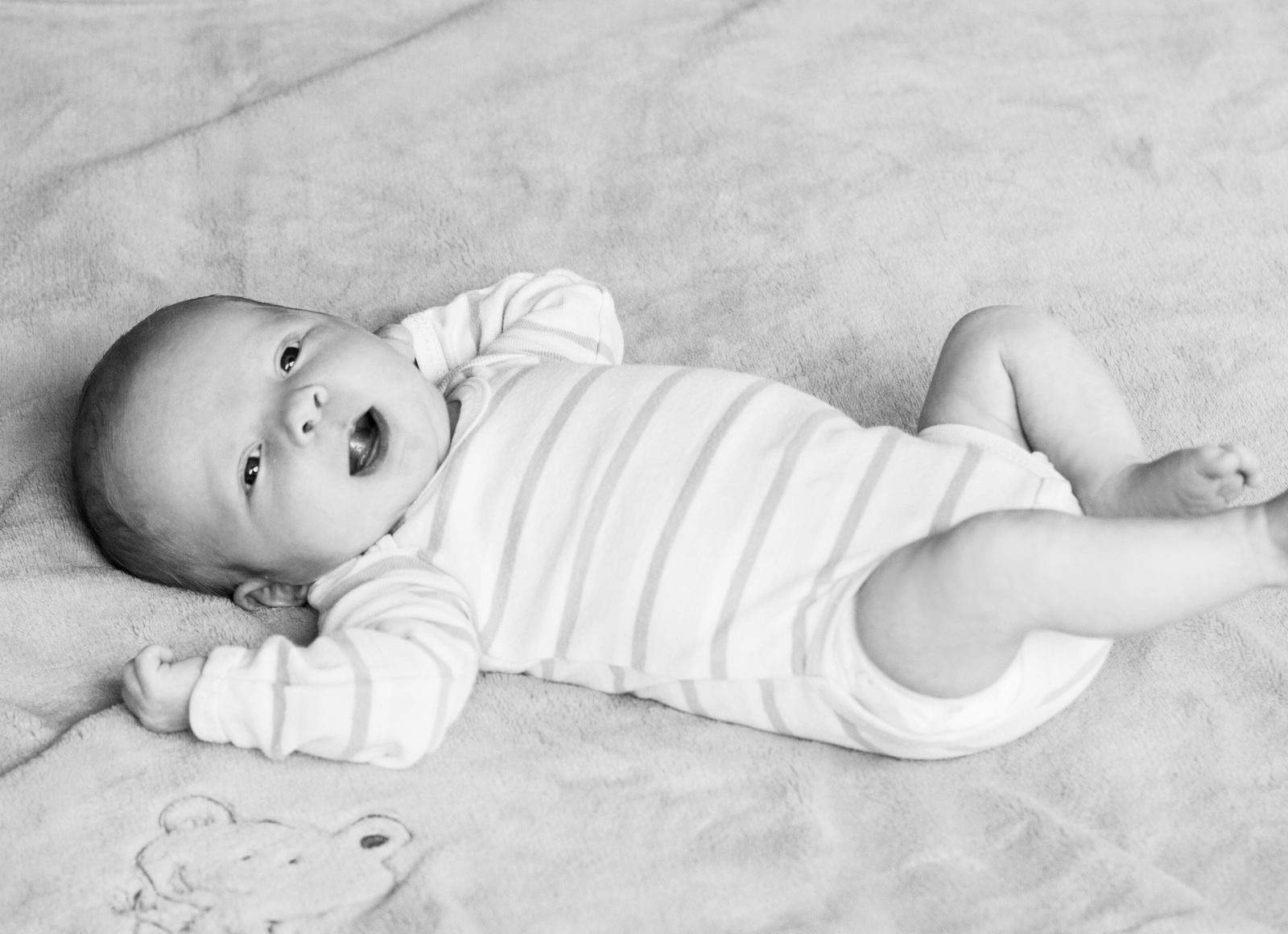 Baby im gestreiften Body liegt lächelnd auf einer Decke – Schwarz-Weiß-Aufnahme