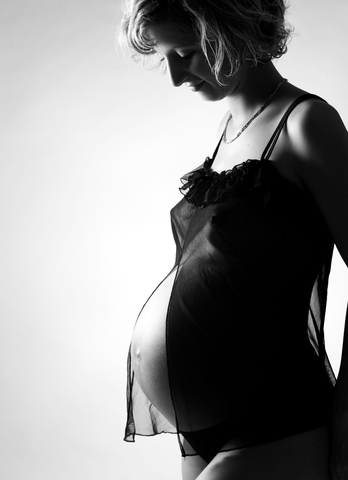 Pregnant woman in profile gazing down at her baby bump — black-and-white portrait