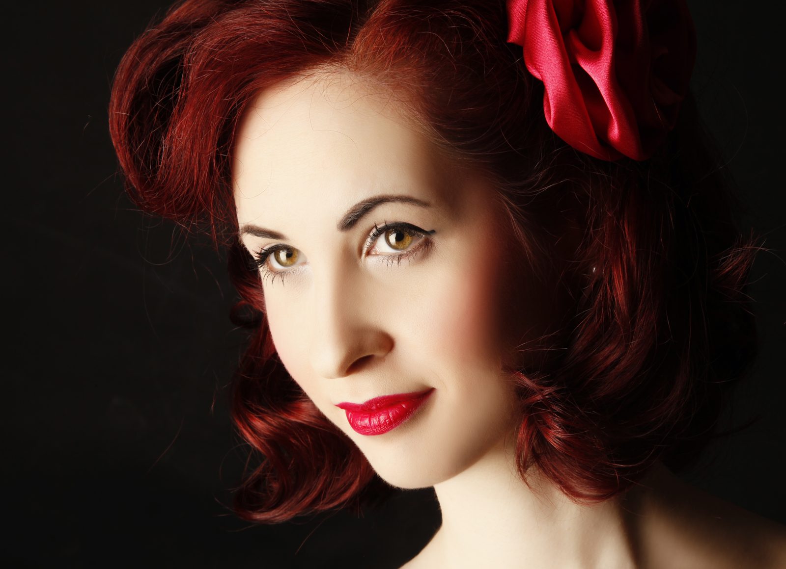 Beauty portrait of a red-haired woman with a red satin bow against a dark background