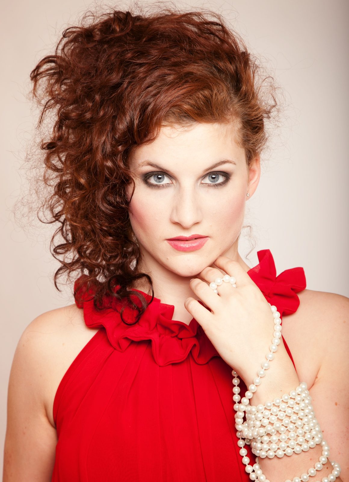 Woman with red curls in a red dress holding a pearl necklace—studio portrait