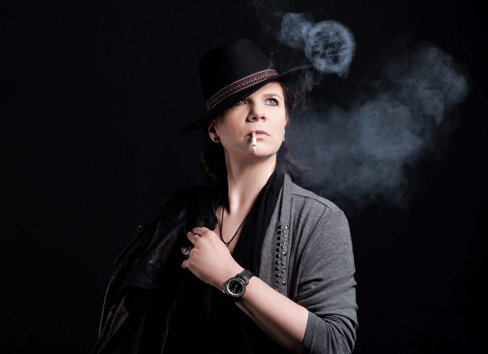 Woman in a hat with a cigarette against a dark background, smoke rising