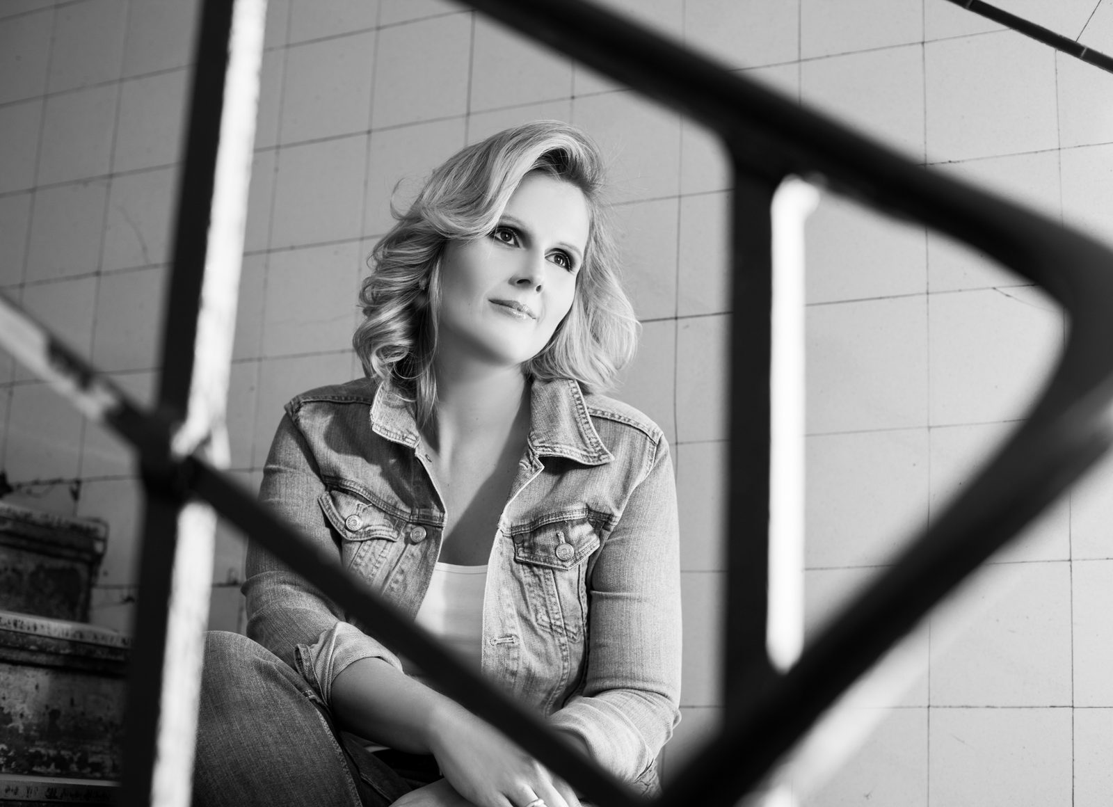 Black-and-white portrait of a woman in a denim jacket seen through a metal frame