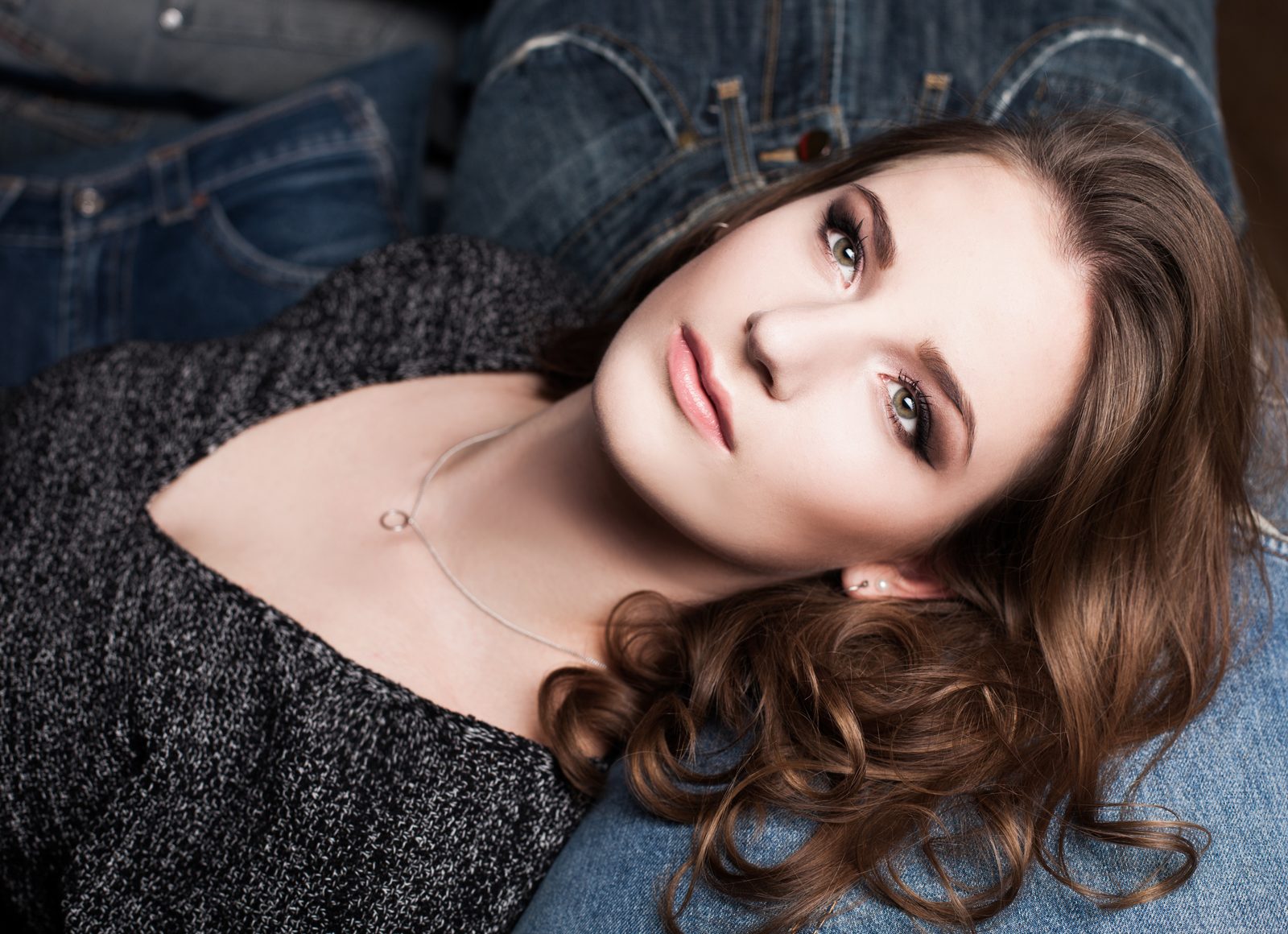 Beauty portrait of a woman with curly hair lying on denim