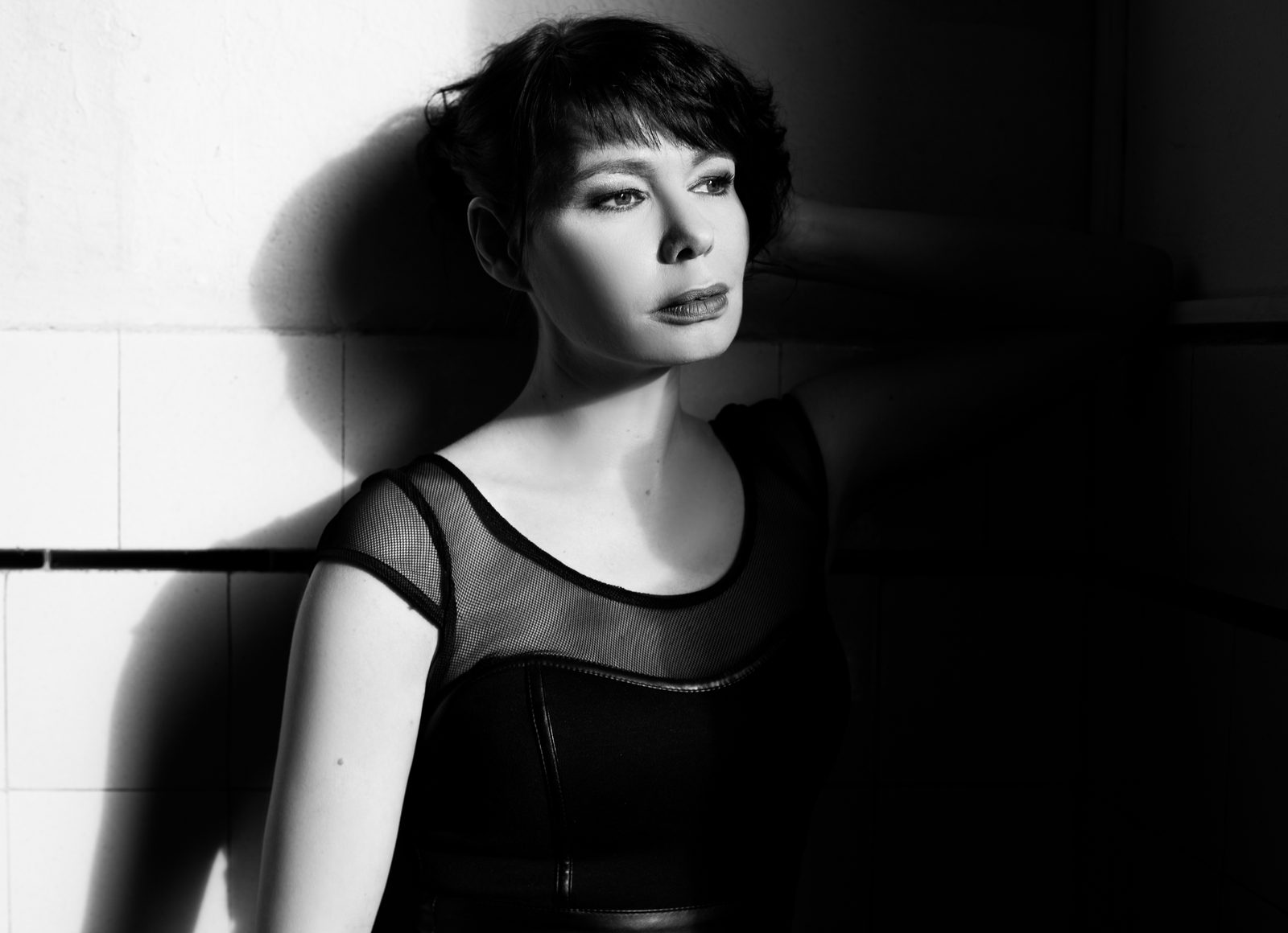 Black-and-white portrait of a woman in dramatic side light against a tiled wall