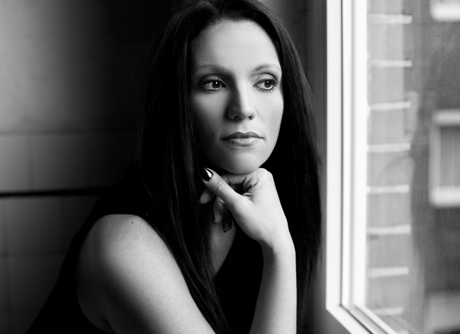 Woman with dark hair gazes thoughtfully out a window—black and white portrait