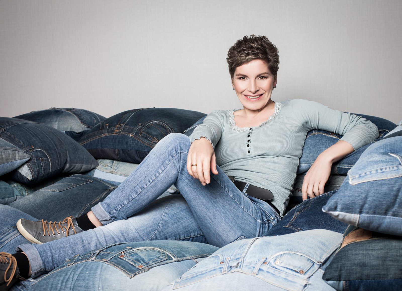 Lächelnde Frau sitzt zwischen Jeans-Kissen im Fotostudio in Hamburg