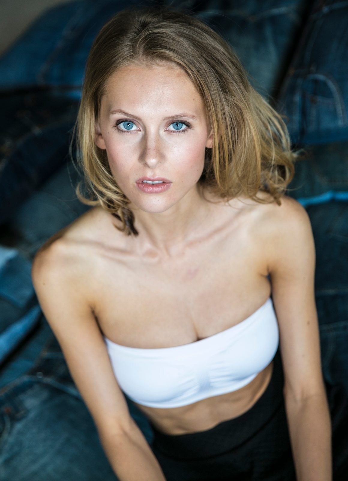 Junge Frau mit blauen Augen im weißen Bandeau-Top vor Jeansstoff-Hintergrund