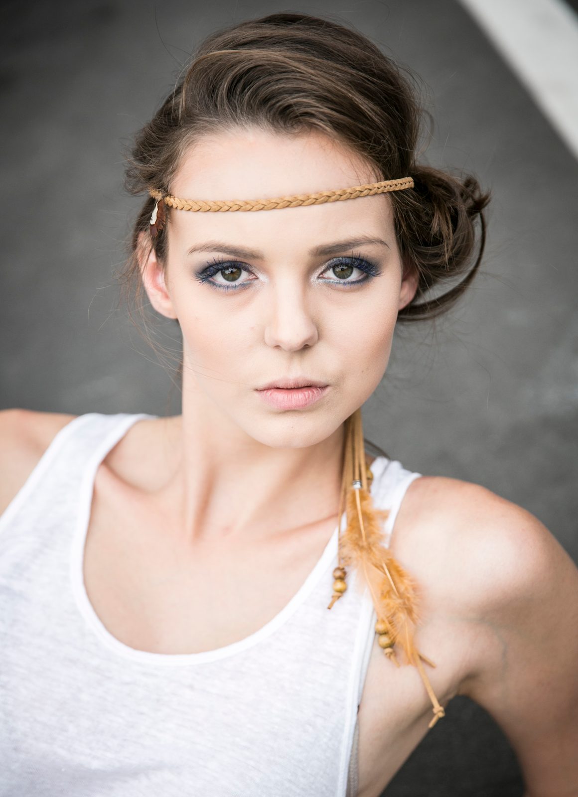 Young woman with braided headband and feather earring looks at camera
