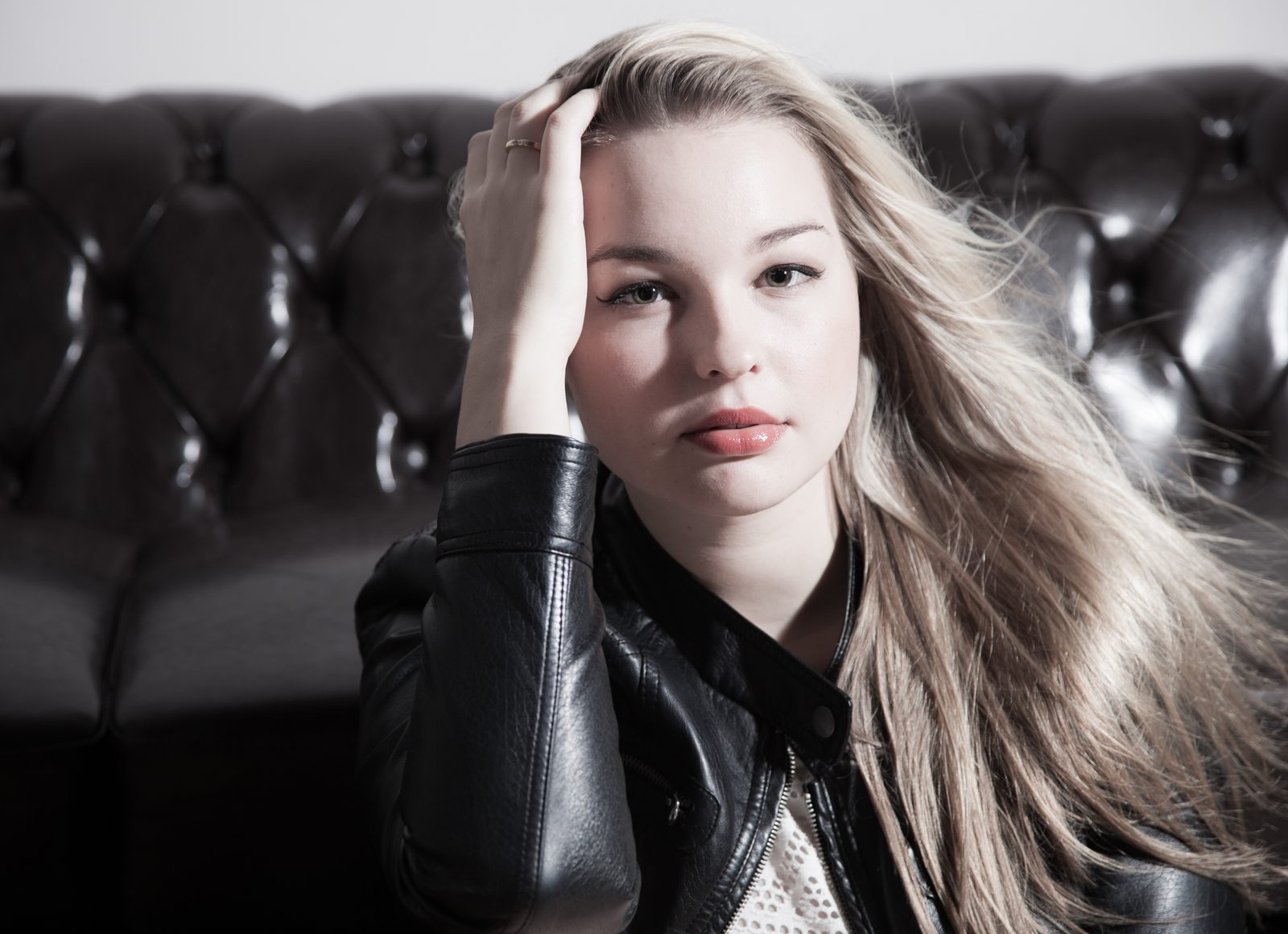 Young woman with blonde hair in a leather jacket against a dark leather sofa