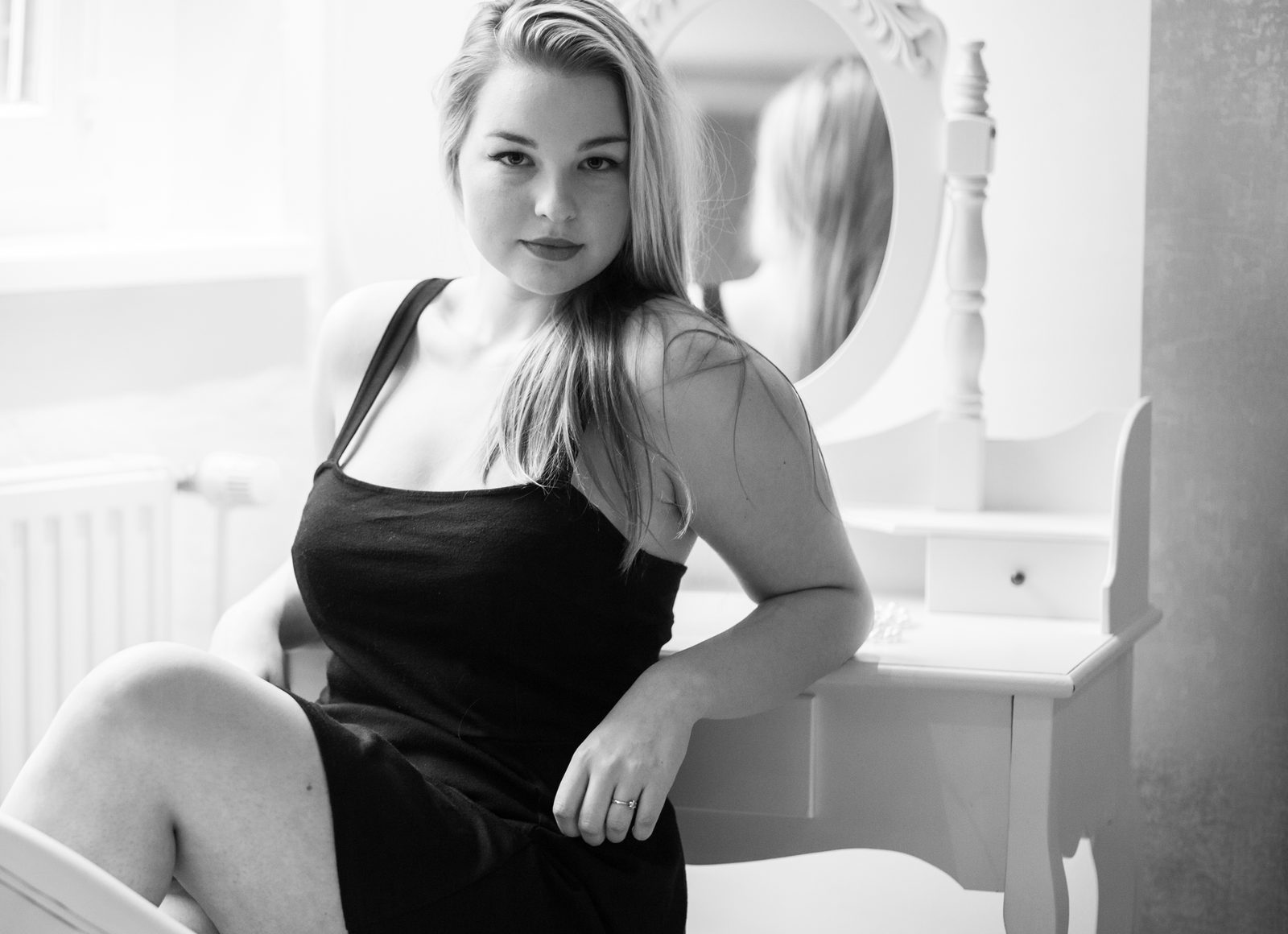 Frau im schwarzen Kleid sitzt vor Schminktisch mit Spiegel – Schwarz-Weiß-Porträt