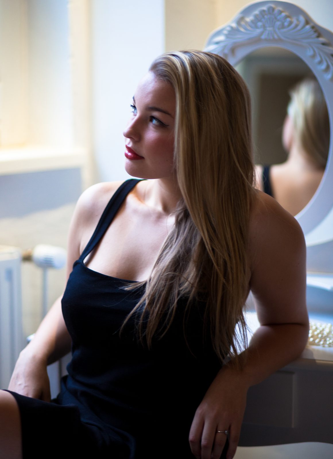 Frau in schwarzem Kleid sitzt vor einem verzierten Spiegel im Fotostudio in Hamburg