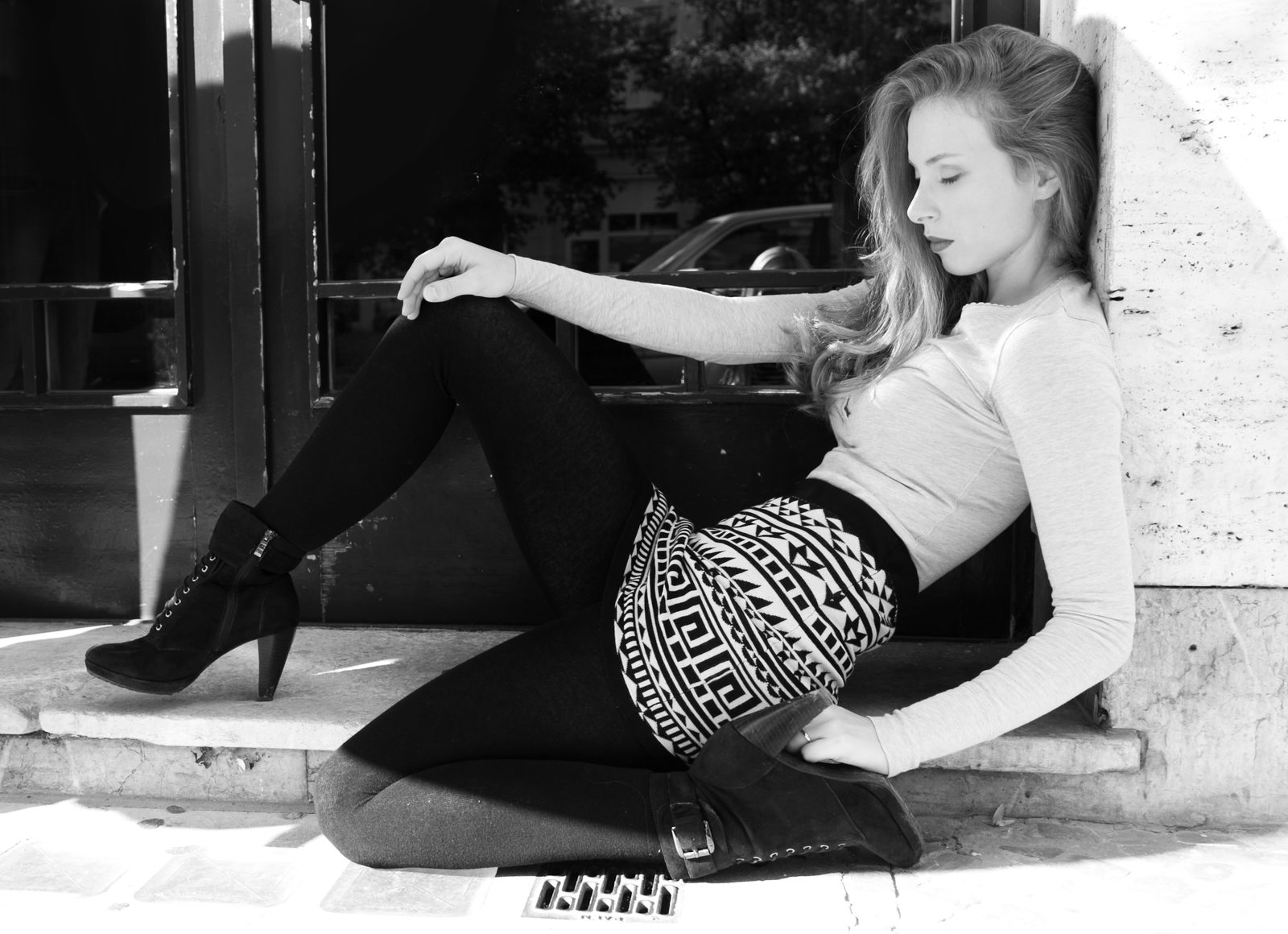 woman sits black-and-white on a doorstep leaning against a stone wall