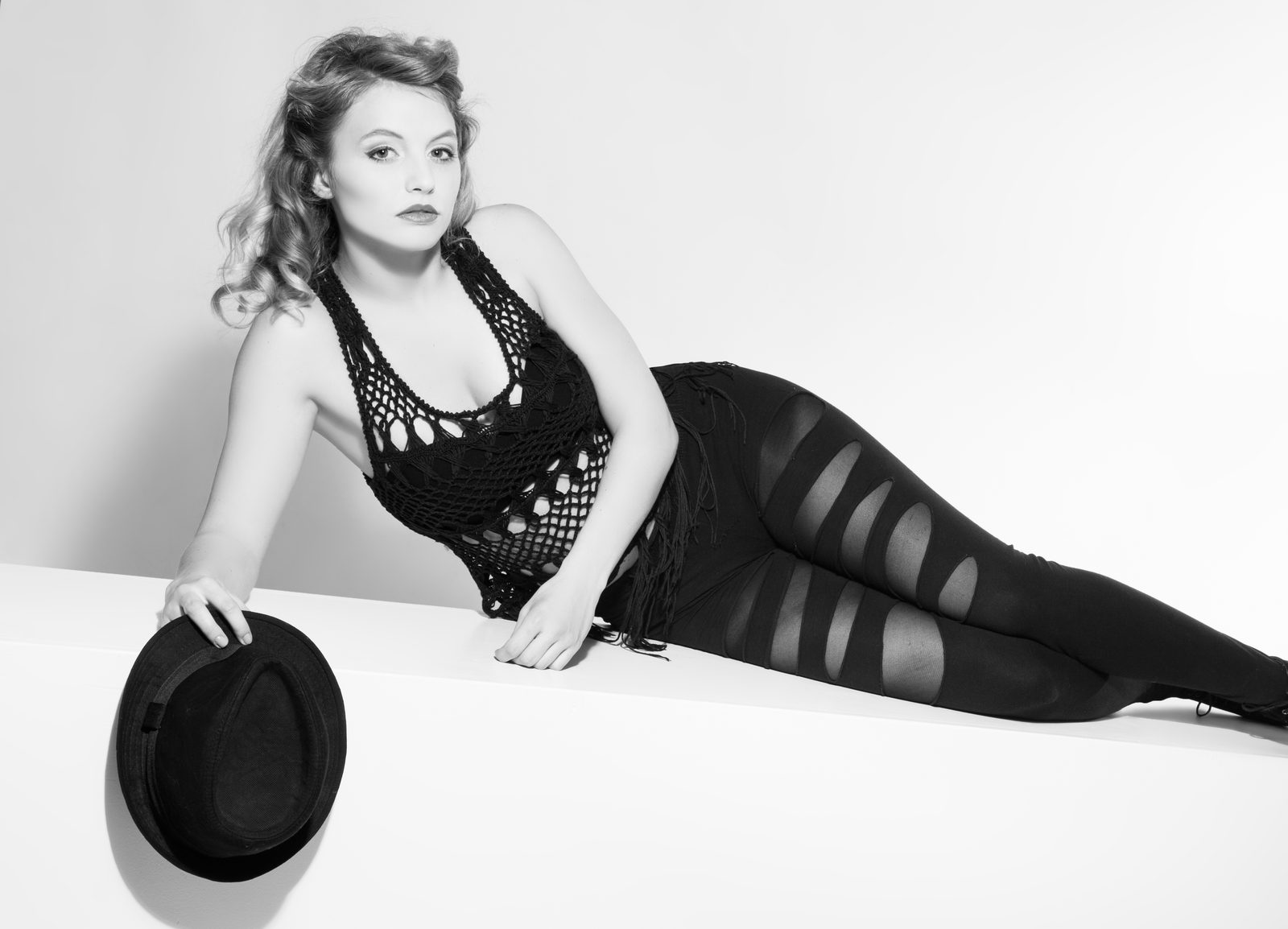 Frau in Schwarz-Weiß-Beauty-Aufnahme liegt mit Hut in der Hand im Fotostudio in Hamburg