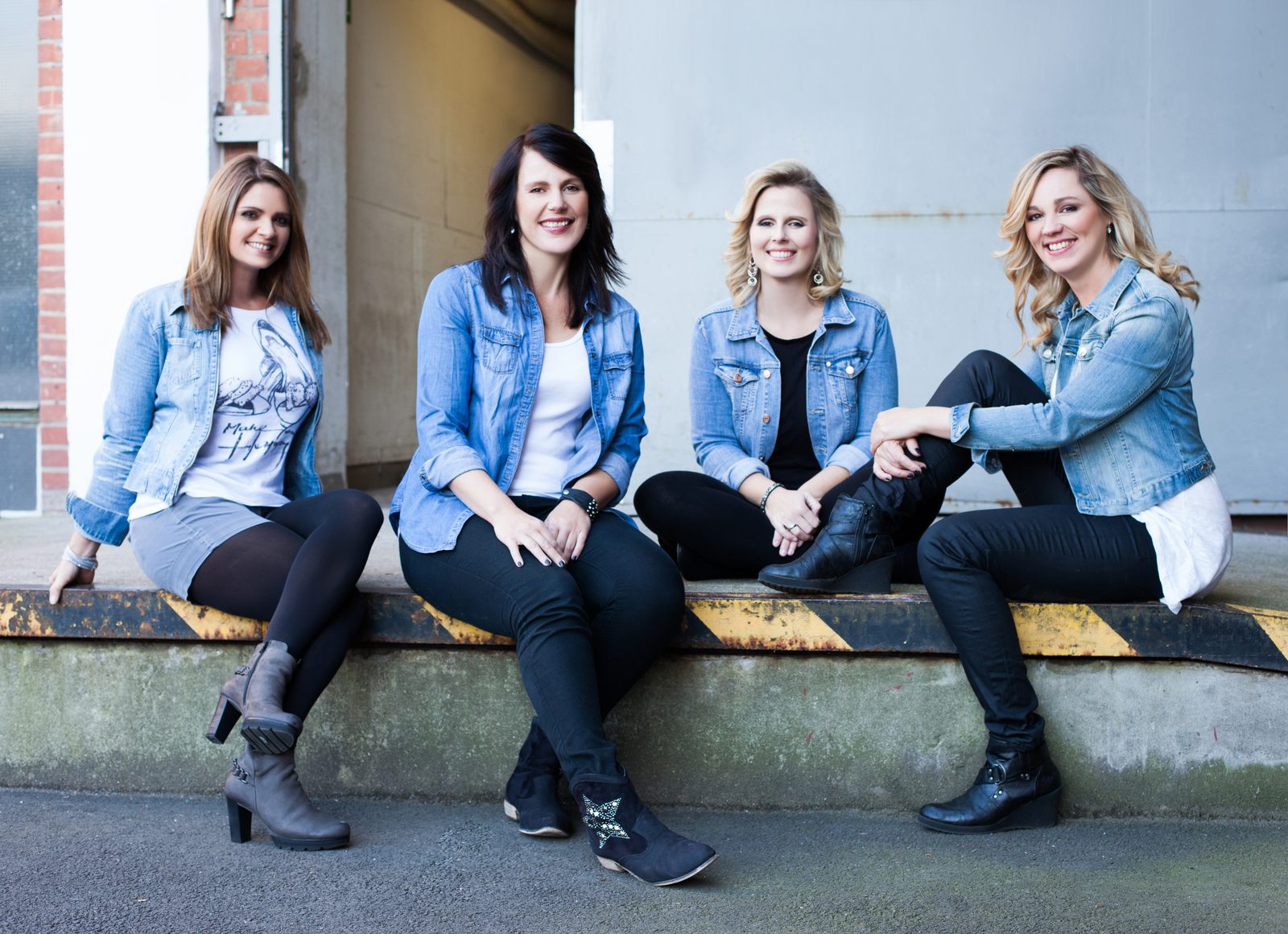 Vier lachende Frauen in Jeansjacken sitzen auf einer Laderampe – Fotoshooting in Hamburg