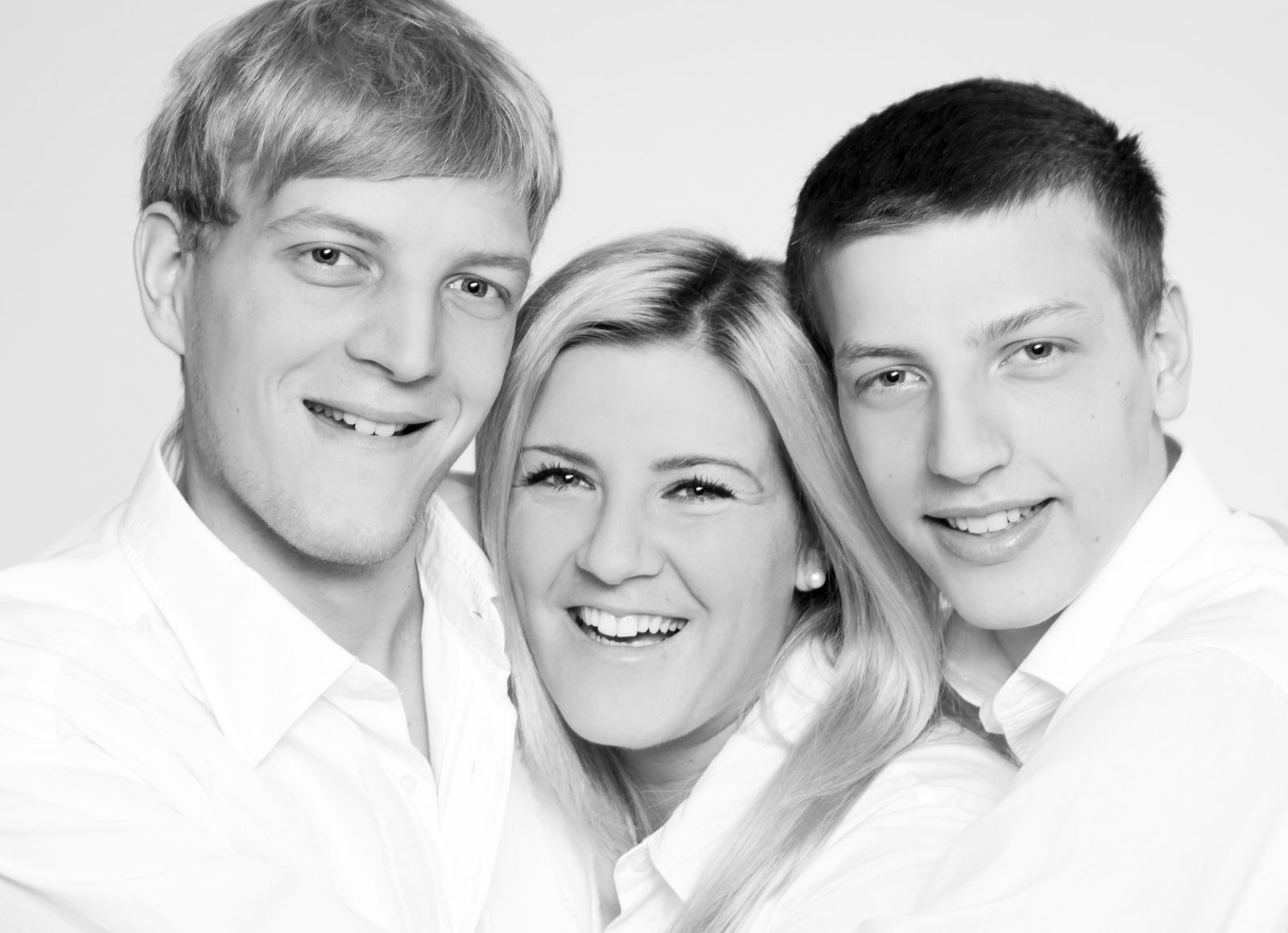 Schwarz-weiß-Porträt von drei lächelnden jungen Erwachsenen in weißen Hemden im Fotostudio in Hamburg