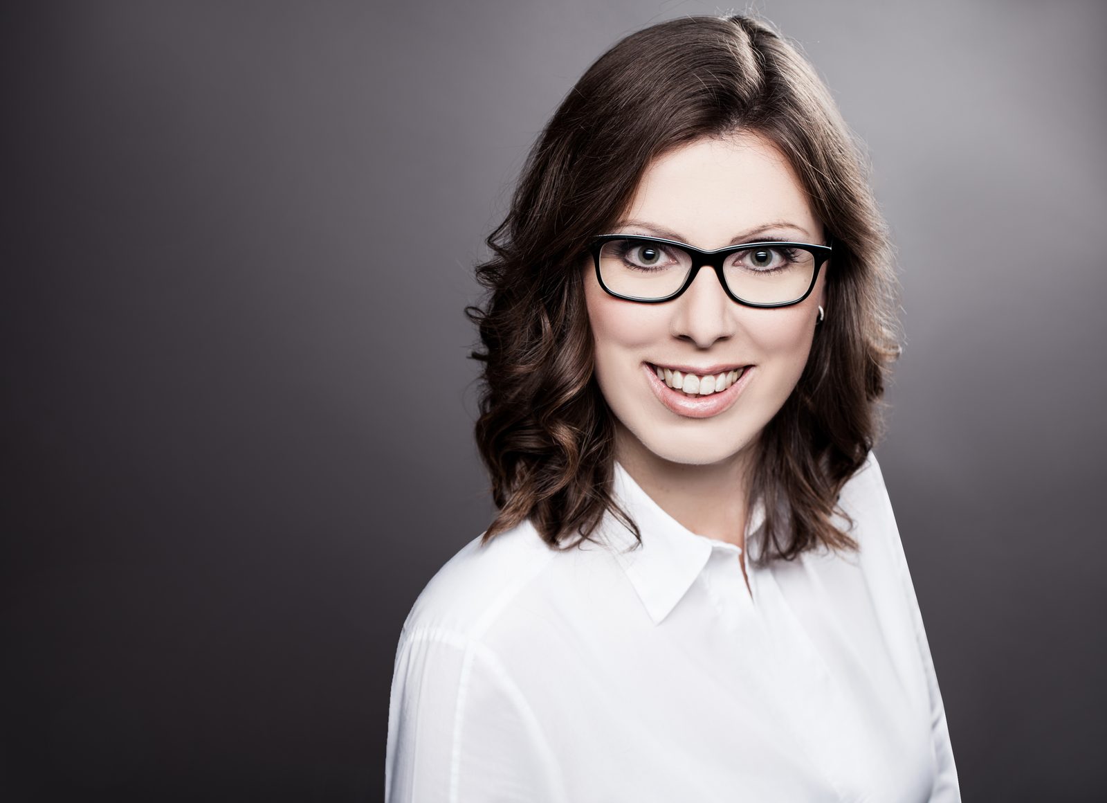 Businessporträt einer lächelnden Frau mit Brille vor dunklem Hintergrund