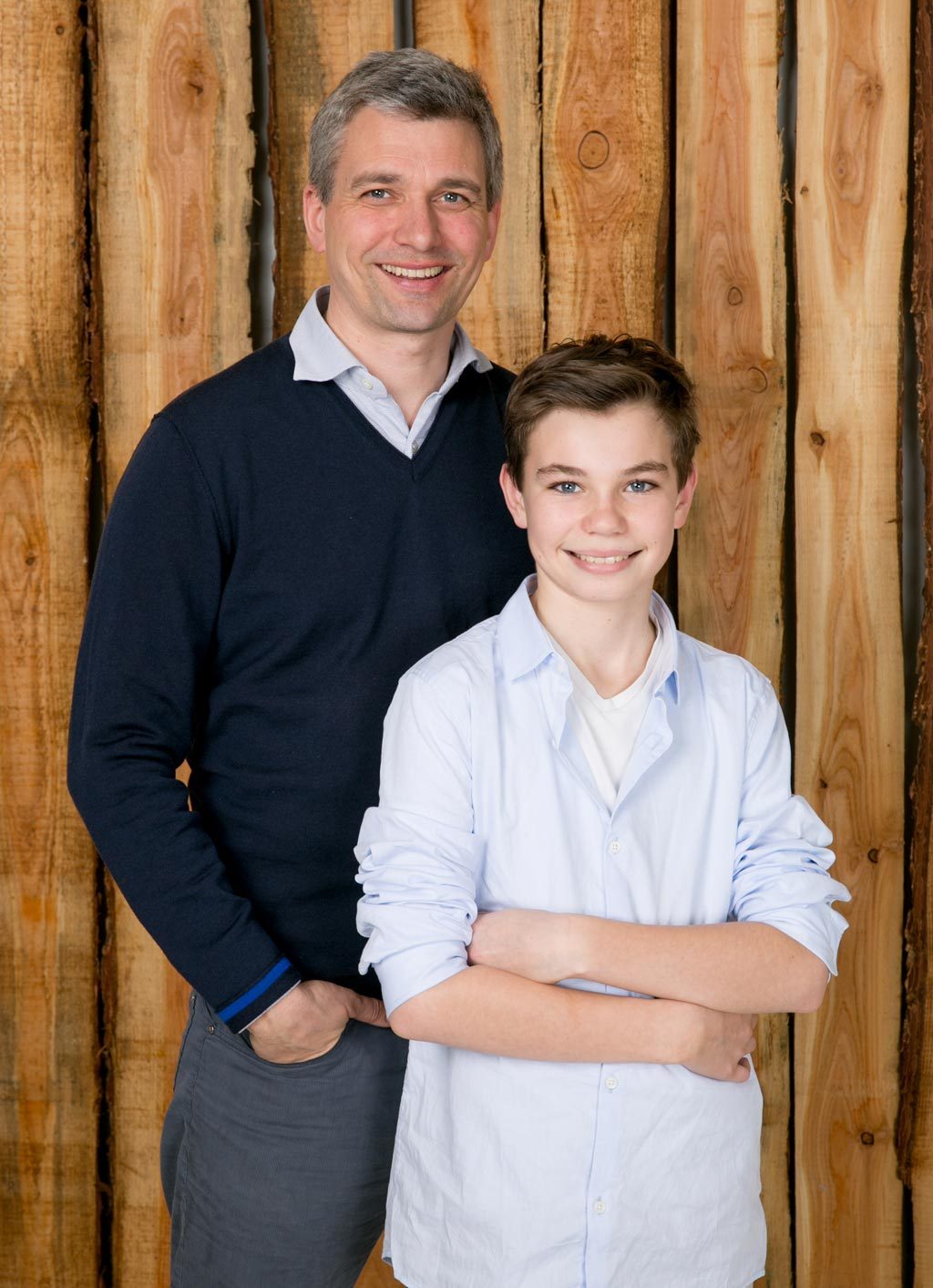 Father and son smiling together against a wooden wall backdrop