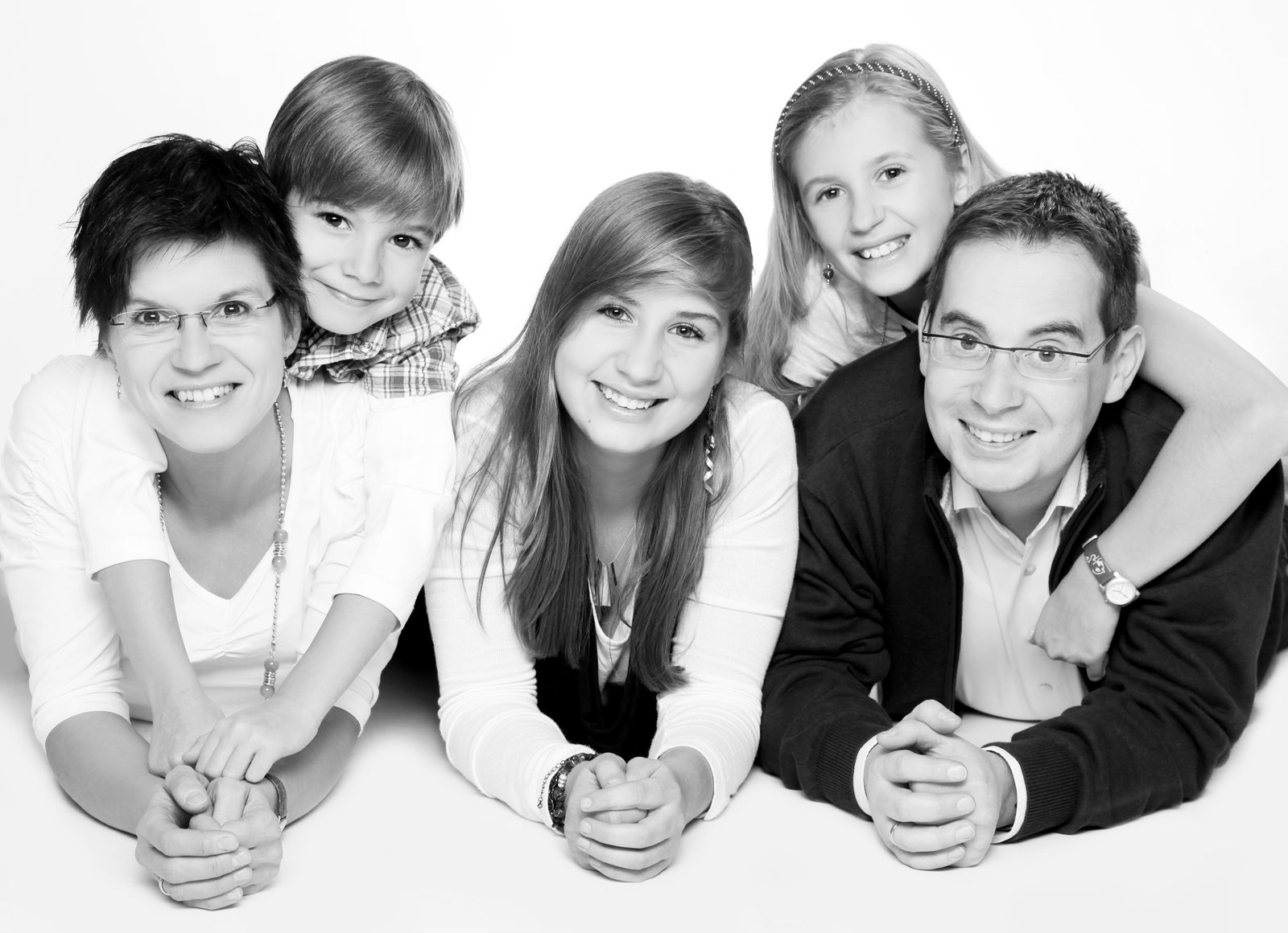 Family of five smiling while lying down in black-and-white studio portrait