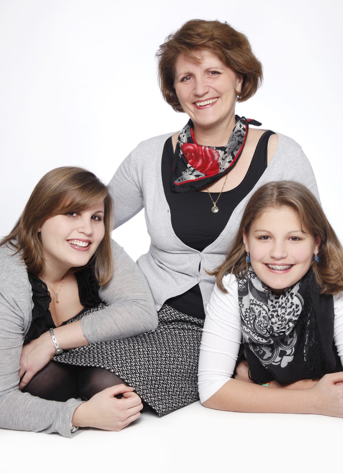 Three smiling generations of a family posing together against a bright studio backdrop