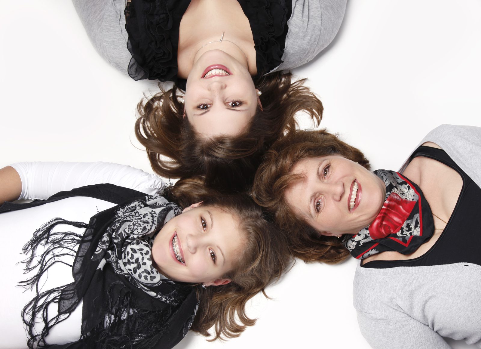 Grandmother, mother, and child lie smiling in a circle on white ground