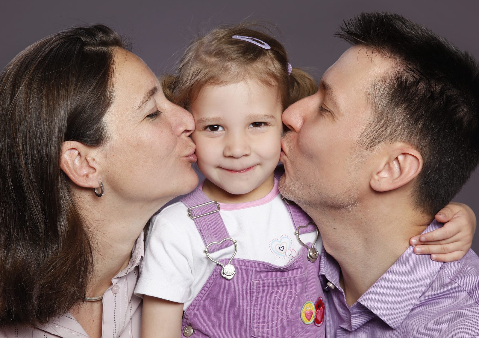 Parents kiss their smiling child's cheeks—family portrait in a studio