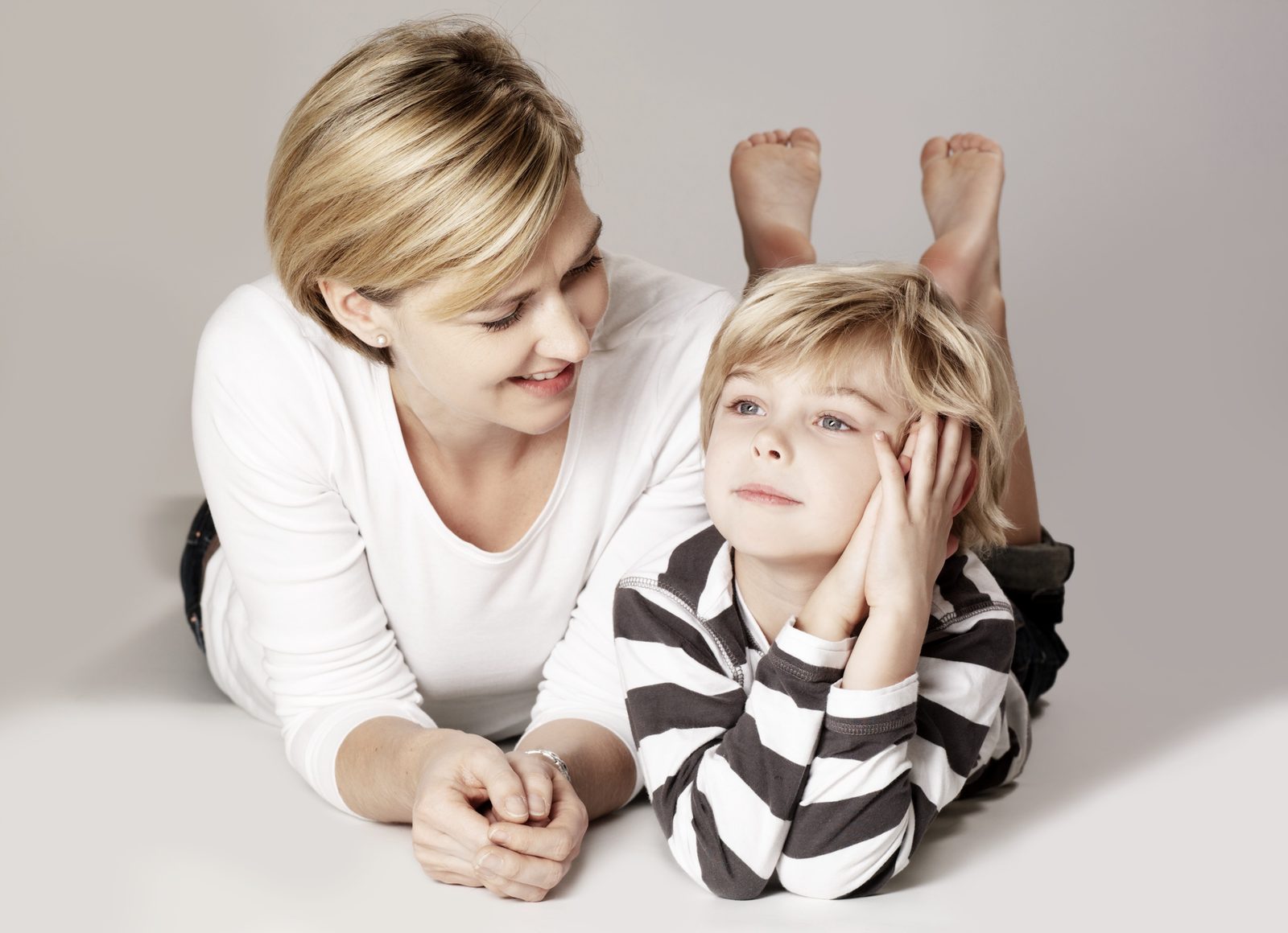 Mother and son lying together, smiling warmly in a bright studio setting