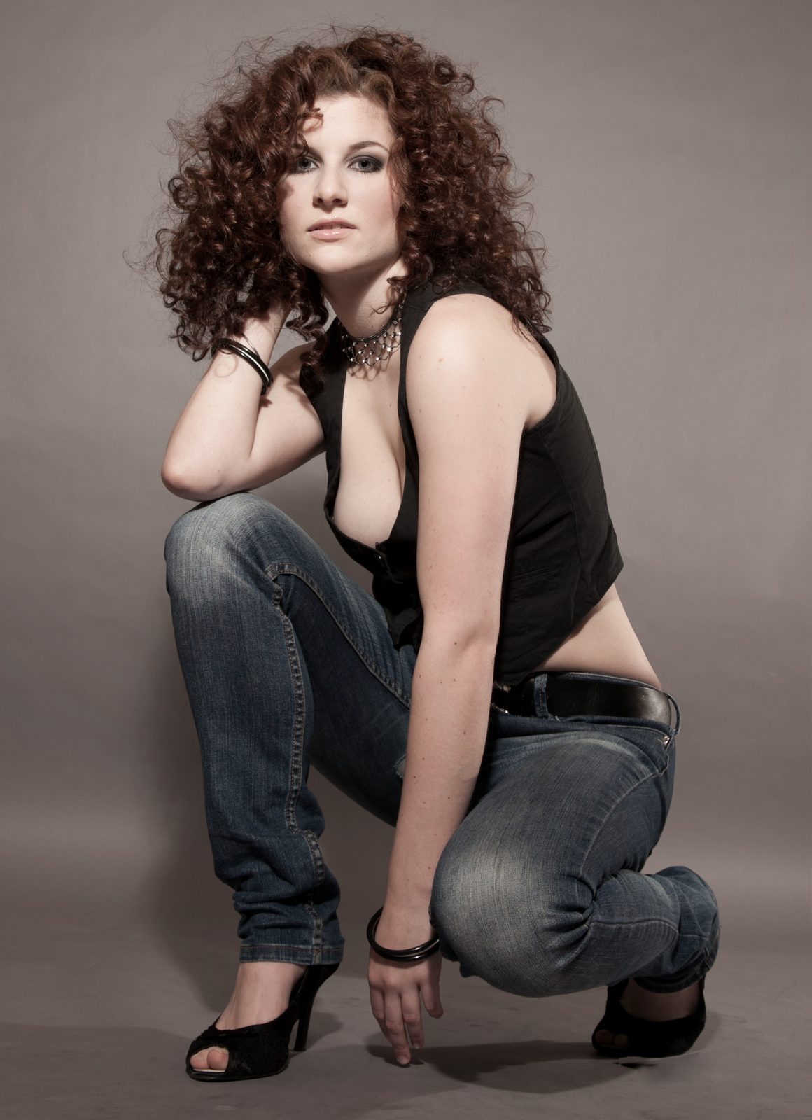 Frau mit Locken posiert kniend im Fotostudio in Hamburg – schwarzes Top und Jeans