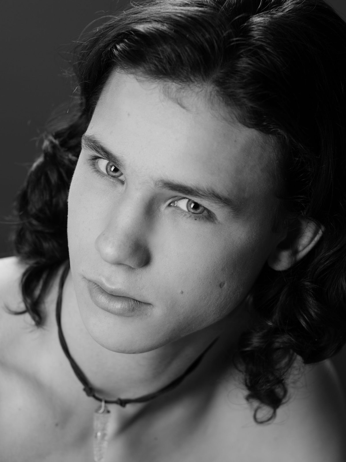 Black-and-white portrait of a young man with curly hair and a necklace