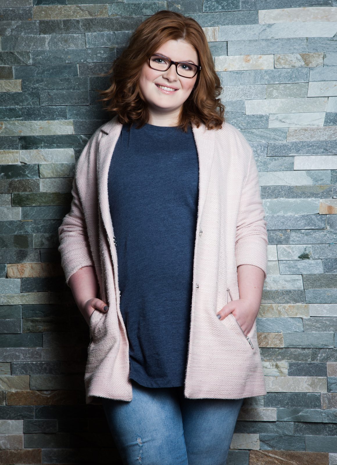 Lächelnde Frau mit Brille und rosa Cardigan vor Steinwand – Fotostudio in Hamburg
