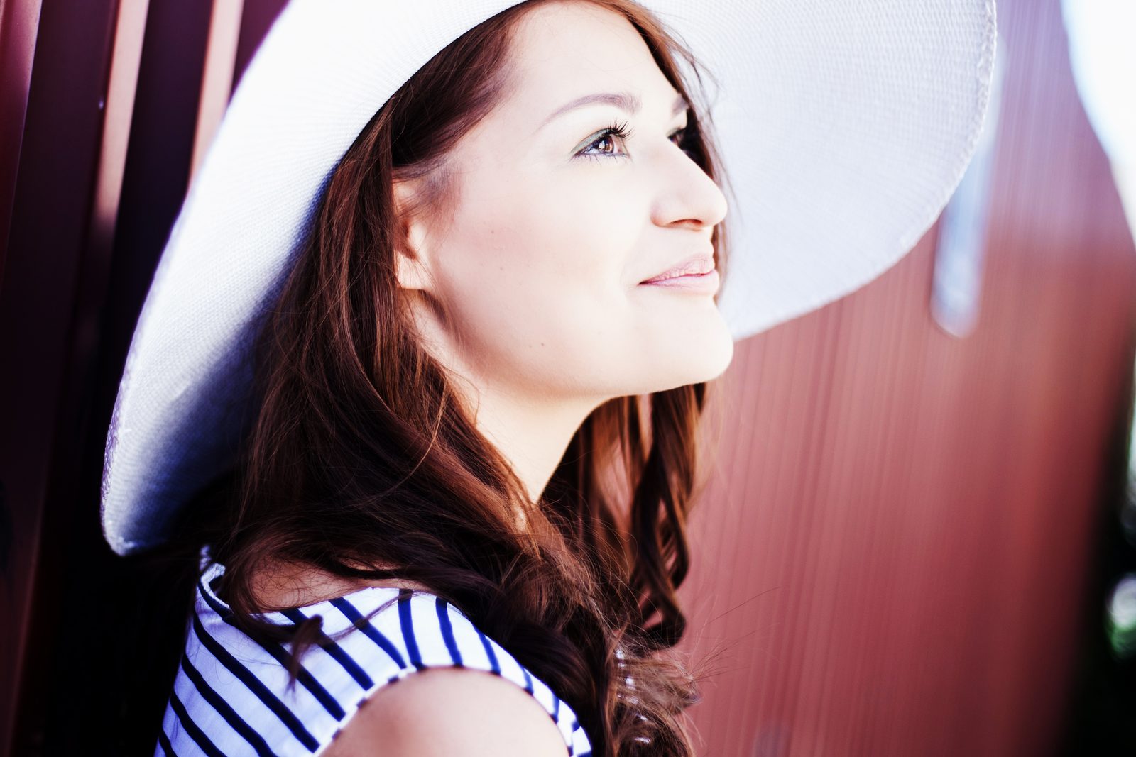 Woman in white sun hat smiles in profile against a reddish backdrop