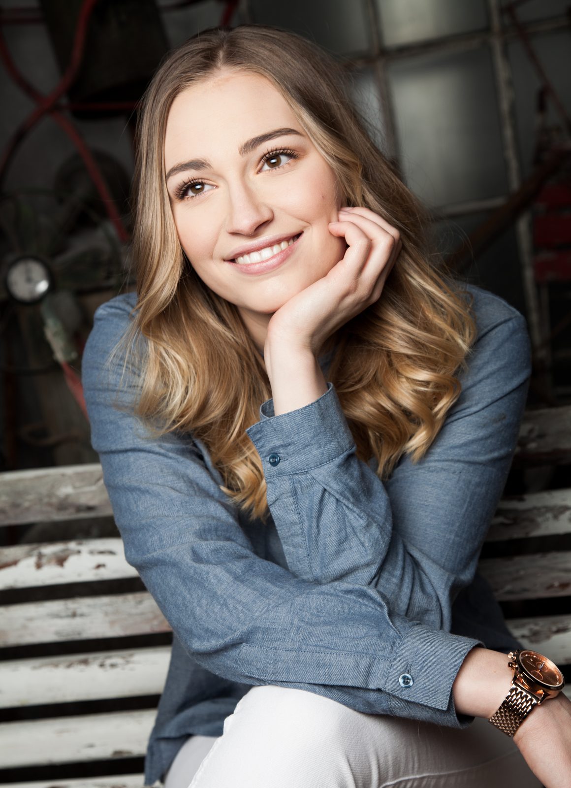 Smiling woman with wavy blonde hair sitting on a wooden bench—portrait shot