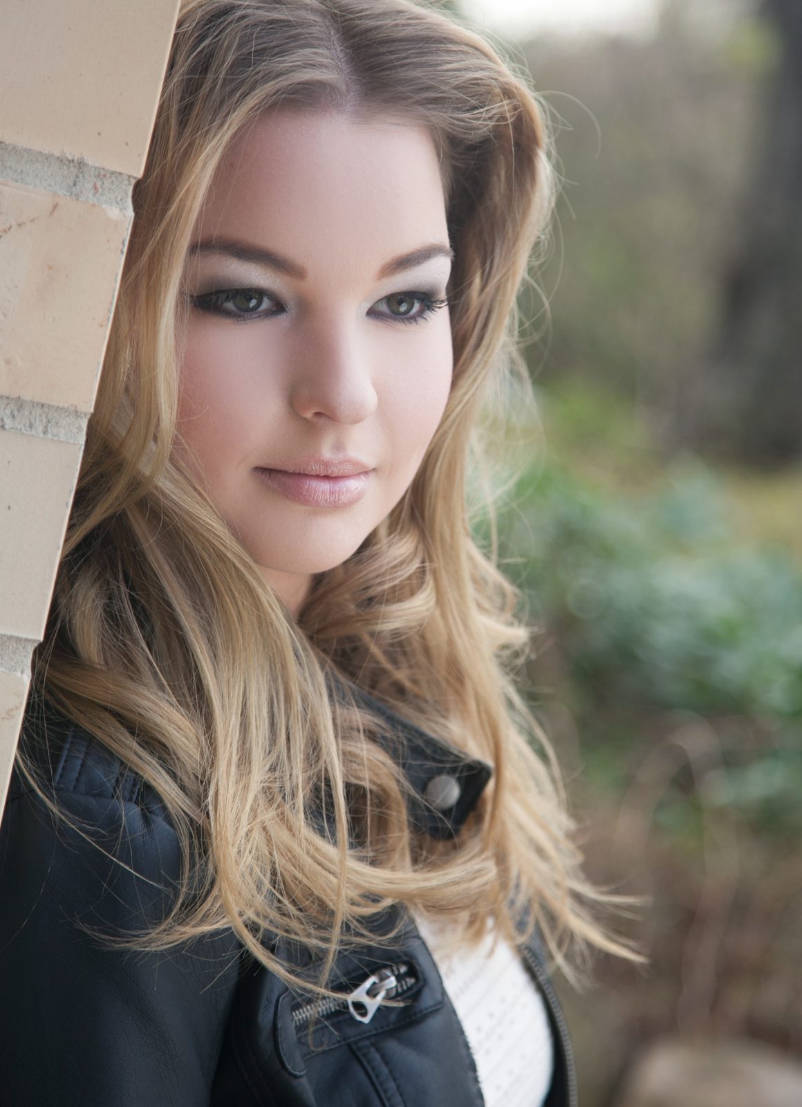 portrait of a woman with wavy blonde hair beside a brick wall outdoors