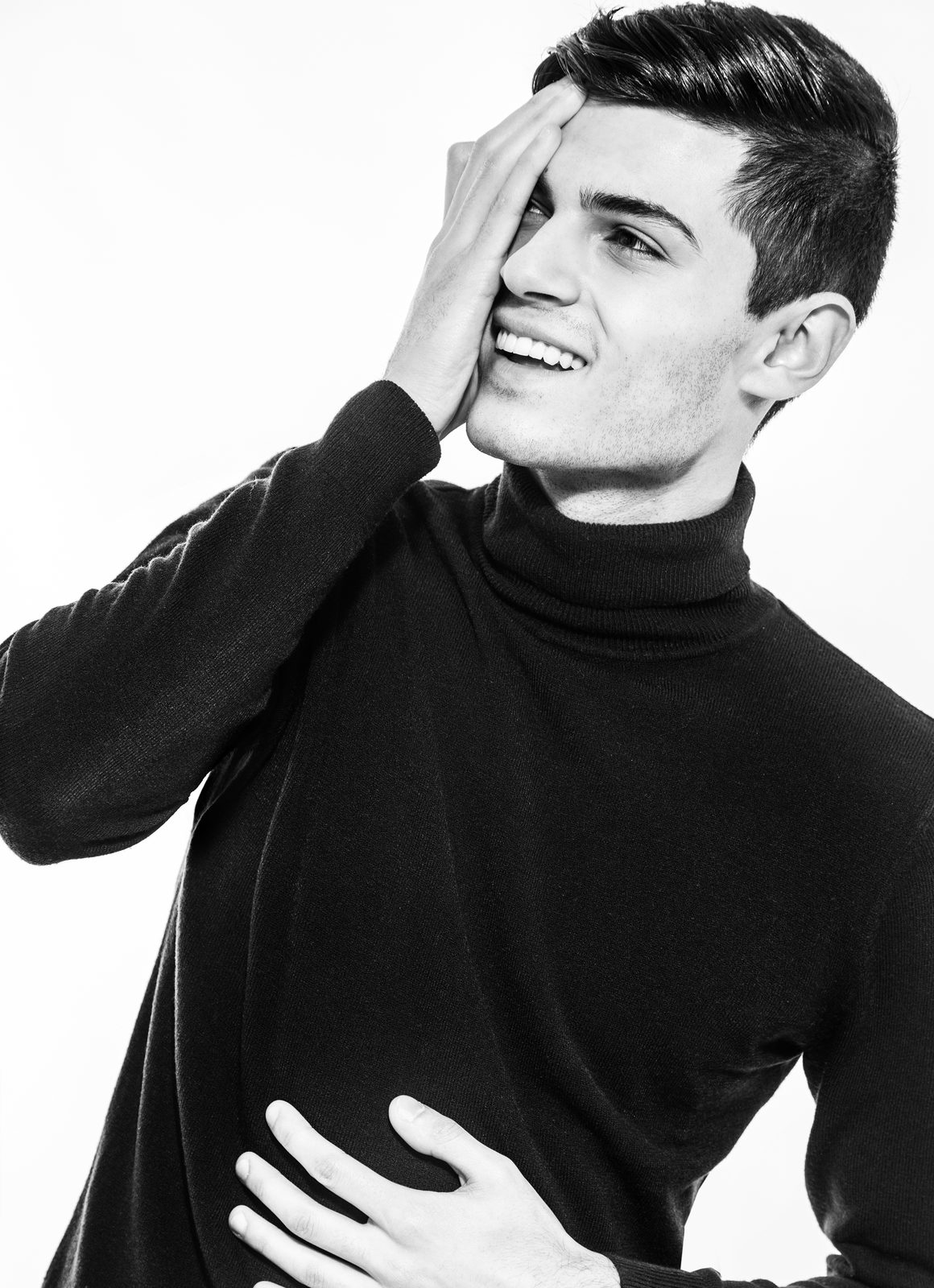 Laughing man in a turtleneck sweater playfully covers one eye with his hand