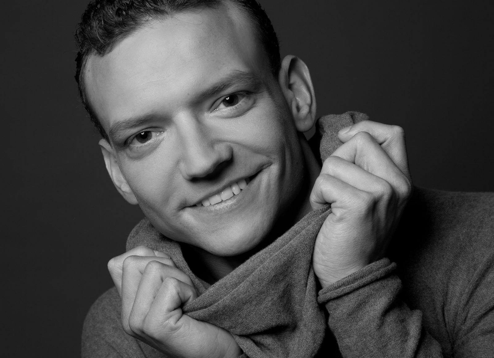 Black-and-white portrait of a smiling man holding up his sweater collar