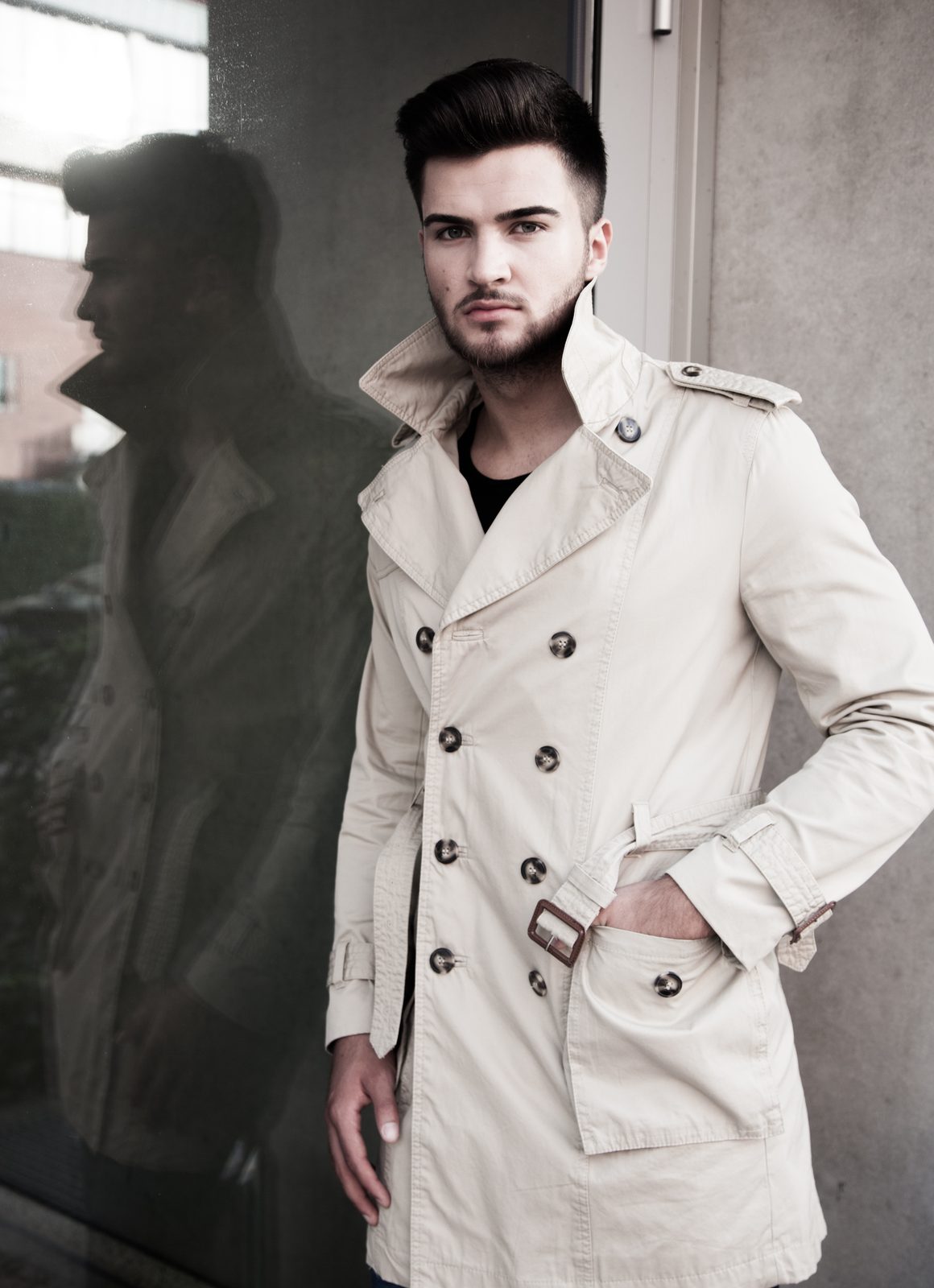 Man in beige trench coat standing before a glass facade in Hamburg