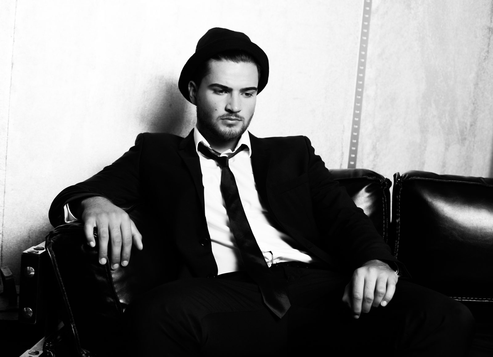 Man in suit and hat sitting thoughtfully on a leather sofa—black and white portrait