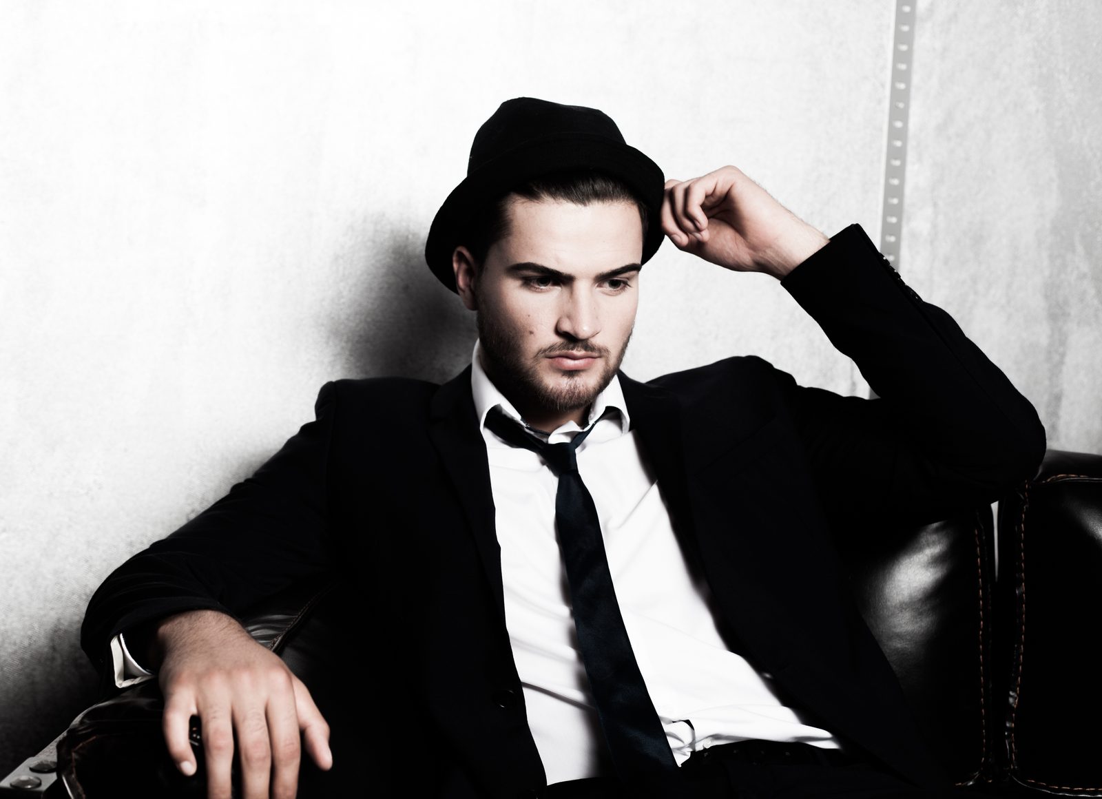 Man in a suit and hat sitting on a leather sofa—studio portrait